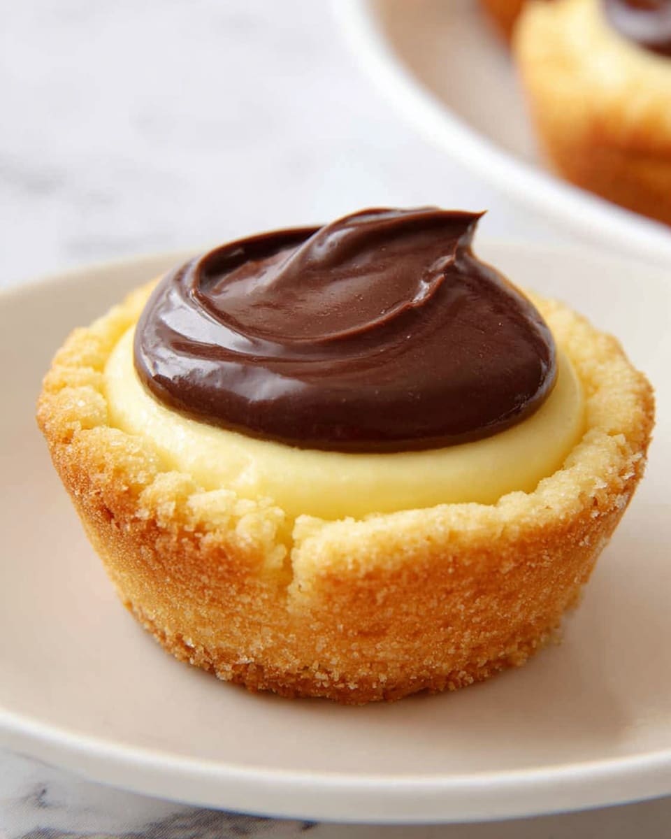 A close-up of a small dessert with three layers on a white plate, set on a white marbled surface. The bottom layer is a golden brown, textured crust that looks crispy and firm, forming a cup shape. Above the crust is a smooth, pale yellow layer that appears creamy and soft, filling the crust fully. The top layer is a thick dollop of shiny, dark brown chocolate, sitting neatly in the center, with gentle swirls adding texture to the glossy surface. Photo taken with an iphone --ar 4:5 --v 7