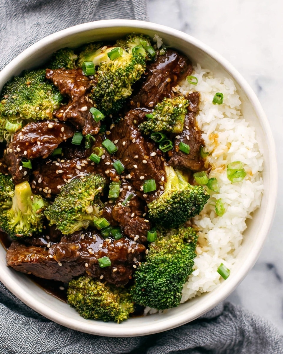 The image shows a white bowl filled with three main layers: on the right side is a soft, fluffy layer of white rice, while most of the bowl is filled with dark brown beef slices mixed with bright green broccoli florets. The beef is covered in a shiny, thick sauce and sprinkled with light tan sesame seeds and chopped green onions, adding texture and color contrast. The broccoli looks tender but crisp, with vibrant green stalks and florets. The dish sits on a soft gray cloth with a white marbled surface beneath. photo taken with an iphone --ar 4:5 --v 7