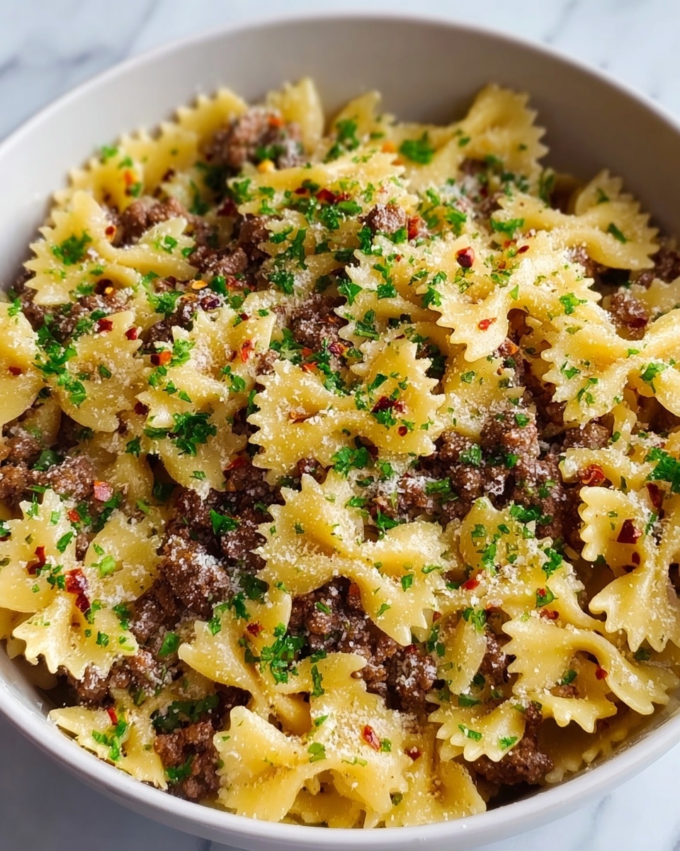 A close-up view of cooked farfalle pasta mixed with browned ground meat in a white bowl. The pasta is yellow with a soft texture, evenly coated with tiny bits of meat scattered throughout. The dish is topped with a sprinkling of chopped green herbs, likely parsley, and a light dusting of grated cheese. Small red chili flakes are also spread across the pasta and meat, adding color contrast. The bowl sits on a white marbled surface, creating a clean and simple setting. Photo taken with an iphone --ar 4:5 --v 7