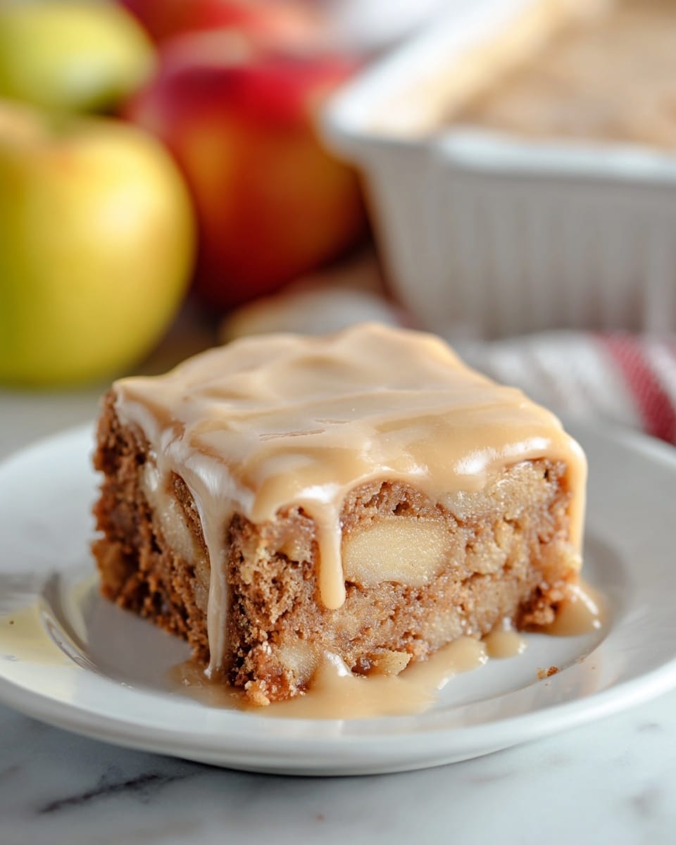 A thick square piece of cake sits on a white plate, showing two main layers. The bottom layer is golden brown, looking moist and textured with bits of apple inside, while the top layer is smooth, creamy light caramel-colored frosting that drips slowly down the sides. The cake edges are slightly crumbly, and the background includes blurred yellow and red apples along with a white baking dish to the right, all set on a white marbled surface. photo taken with an iphone --ar 4:5 --v 7