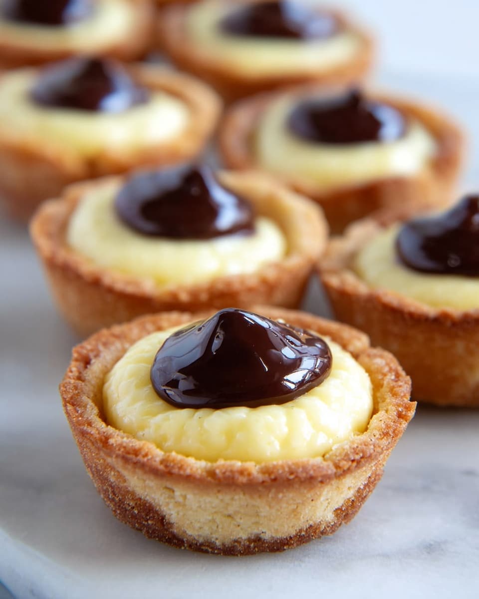 The image shows two rows of mini tarts placed on a white marbled surface. Each tart has three distinct layers: the bottom layer is a golden-brown cookie crust that looks crispy; above that is a creamy, pale yellow filling with a smooth texture; on top of the filling is a small dollop of shiny, dark brown chocolate ganache, creating a glossy finish. The tarts are lined up neatly, with the focus on the front tart, and the background tarts gently blur as they recede. photo taken with an iphone --ar 4:5 --v 7
