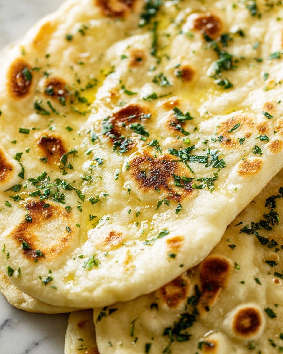 A close-up view of flatbread showing one large piece with a light golden color and soft texture. The flatbread has multiple small browned spots spread across its surface, indicating it was cooked on a hot pan. It is topped with finely chopped green herbs scattered evenly around, and a light layer of shining melted butter giving a moist look. The background shows more pieces of flatbread stacked slightly under the top one, all placed on a white marbled texture. photo taken with an iphone --ar 4:5 --v 7