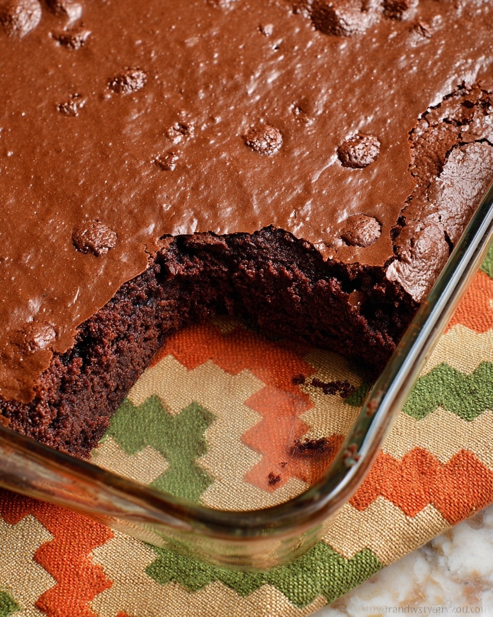 A close-up image of a single-layer chocolate brownie in a square glass baking dish, showing one large piece missing from the bottom right corner. The brownie has a smooth, shiny, slightly cracked chocolate surface with small, uneven bumps and a dense, moist, darker chocolate inside. The baking dish rests on a colorful chevron-patterned cloth with shades of green, orange, and cream, all set against a white marbled texture surface. photo taken with an iphone --ar 4:5 --v 7