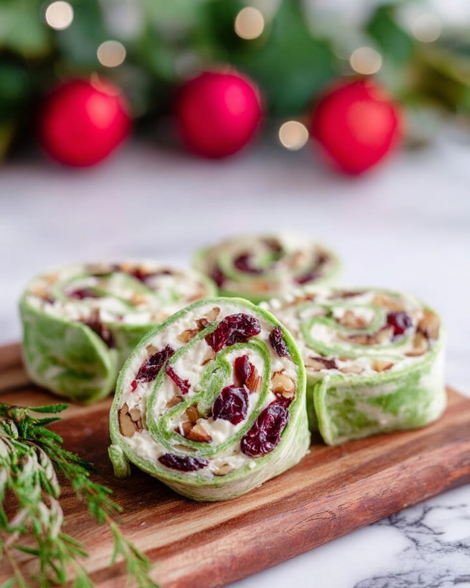 The image shows four spiral wraps placed on a wooden board. Each wrap has a green outer layer that looks soft and thin. Inside, there is a creamy white layer mixed with bits of dark red, likely dried cranberries, and small light brown pieces, possibly nuts. The wraps are thick with visible swirls of the green and white layers. In the background, there are blurred green leaves and red round decorations, with some white highlights, all set on a white marbled surface. A small green herb is placed near the wraps. Photo taken with an iphone --ar 4:5 --v 7