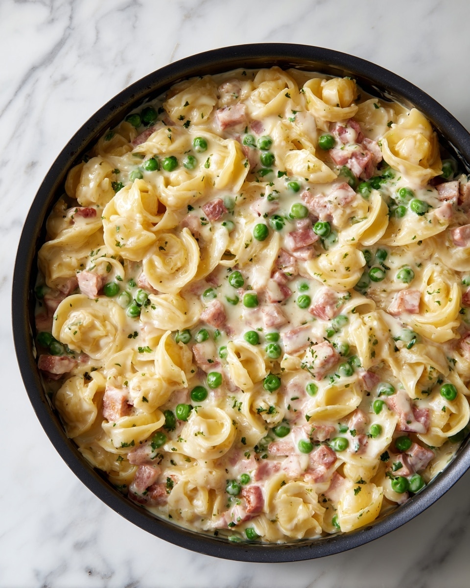 The image shows a close-up view of a creamy pasta dish in a black pan, placed on a white marbled surface. The dish has three visible layers of ingredients: the base layer consists of curly egg noodles that are light yellow and soft in texture; the middle layer has small pieces of pinkish cooked meat and bright green peas mixed evenly throughout; the top layer is a smooth, white creamy sauce that coats the pasta and vegetables gently. The overall color mix is pale yellow with pops of green and pink, giving the dish a rich and hearty look. Photo taken with an iphone --ar 4:5 --v 7