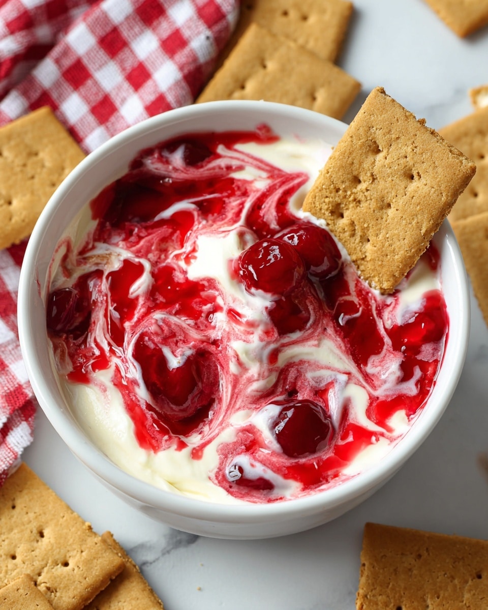 The image shows a white bowl filled with a creamy white base layer mixed with vivid red swirls of cherry sauce, creating a marbled effect on the top. The creamy texture looks smooth and soft, while the red cherry sauce layer appears glossy with pieces of cherries visible, adding a slightly chunky texture. Two rectangular golden-brown graham crackers are inserted into the dessert, one standing upright near the bowl edge and the other lying flat on the side, both showing a slightly rough, crumbly texture. The bowl is placed on a white marbled surface, with more graham crackers scattered partially under it and a red and white checkered cloth in the background. photo taken with an iphone --ar 4:5 --v 7