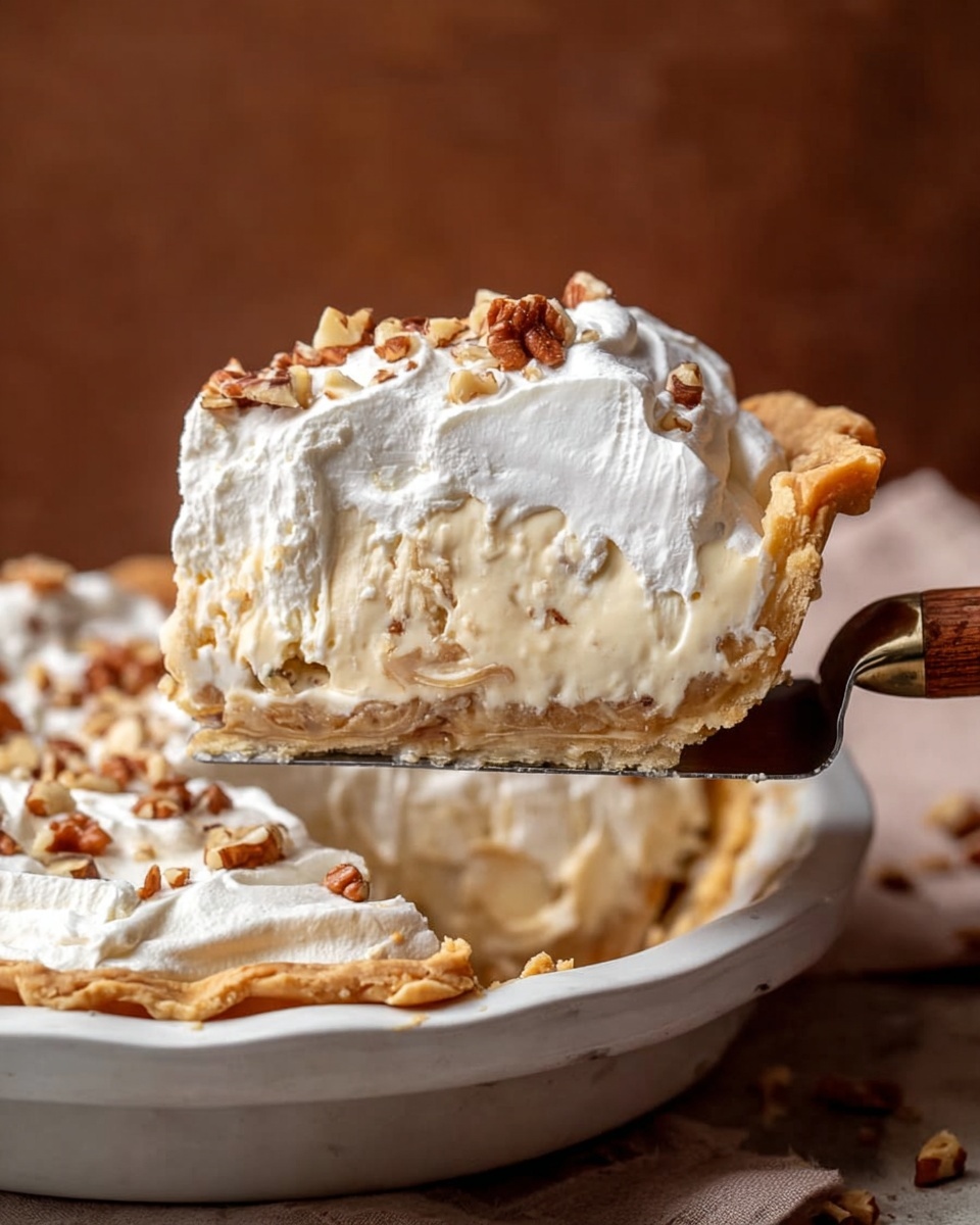 A slice of pie is being lifted from a white pie dish on a white marbled surface. The pie has three layers: a golden-brown flaky crust at the bottom and edges, a thick creamy filling with bits of nuts mixed in the middle, and a thick, fluffy white topping of whipped cream sprinkled with small pieces of chopped nuts. The background is a warm brown color, and the slice is held by a spatula with a wooden handle. photo taken with an iphone --ar 4:5 --v 7