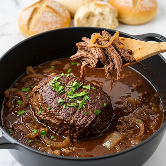 A black pot filled with a dark brown stew containing a large piece of shredded beef in the center, topped with chopped green herbs and cooked onions. The thick sauce surrounding the meat has medium sized onion pieces visible throughout. A wooden spoon is lifting a portion of the beef from the stew. In the blurred background, round pieces of light-colored bread with visible crumb texture sit on a white marbled surface. photo taken with an iphone --ar 4:5 --v 7