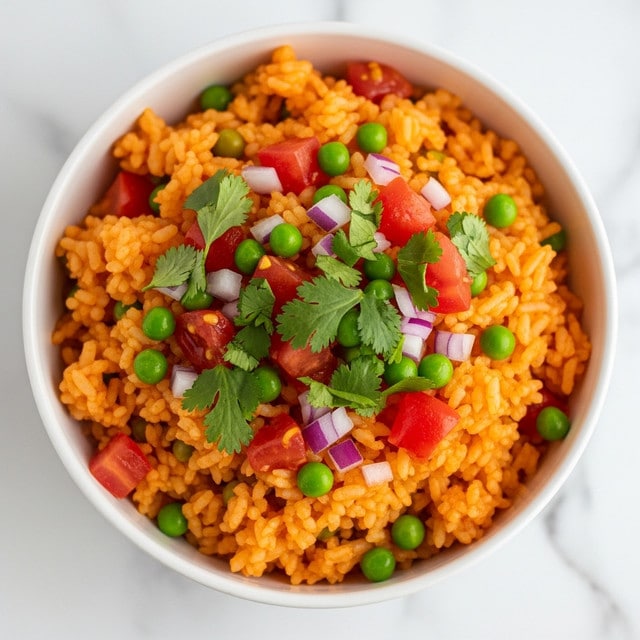 A close-up of a bowl filled with orange-colored spiced rice mixed with small chunks of red tomato and green peas, topped with chopped fresh green cilantro leaves and small pieces of purple onion scattered on top, the bowl is white, and the background is a white marbled texture. photo taken with an iphone --ar 4:5 --v 7