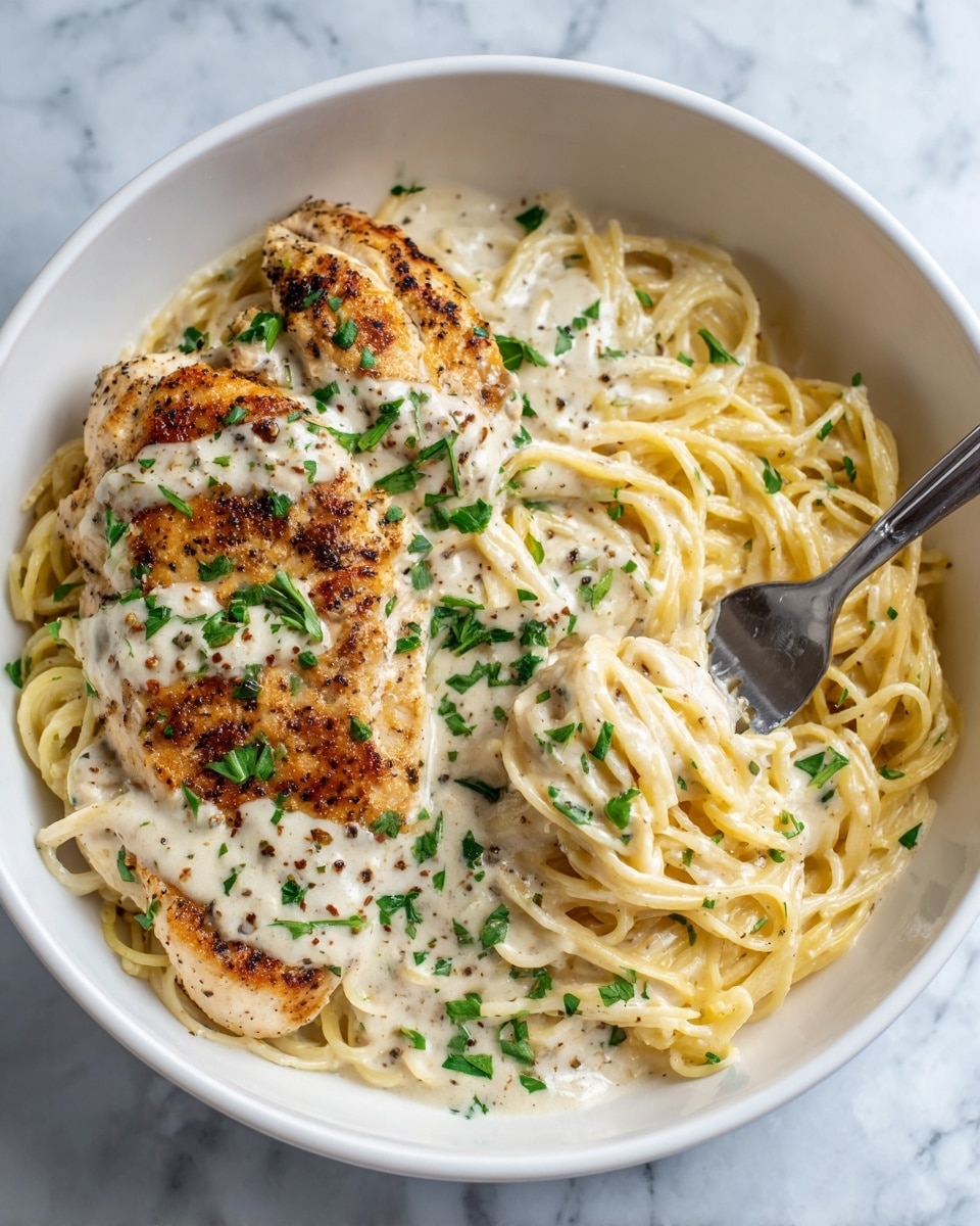 A white bowl filled with a base layer of light yellow spaghetti, coated lightly with creamy sauce, topped by two golden brown grilled chicken breasts covered in thick creamy sauce with specks of black pepper. Fresh green parsley pieces are sprinkled over the chicken and pasta, adding a pop of color. A silver fork is lifting some spaghetti on the right side of the bowl. The bowl is placed on a white marbled surface. photo taken with an iphone --ar 4:5 --v 7