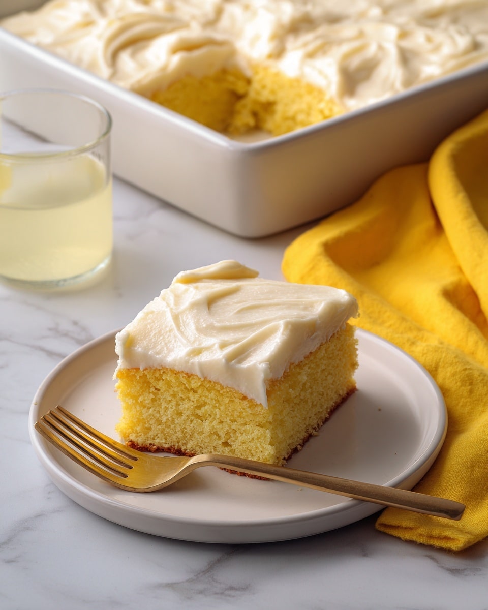 The image shows a single square piece of yellow cake with creamy white frosting on top, placed on a white plate. The cake slice reveals a soft, spongy texture inside and a slightly darker golden edge. The thicker layer of smooth, swirled frosting covers the top evenly. Next to the plate is a gold fork resting at the left side of the cake. In the background, a white rectangular baking pan holds the rest of the cake with a large piece missing. The cake in the pan has the same thick, swirled frosting and golden crumb, sitting on a white marbled surface. Two clear glasses with a light yellow beverage are also partially visible behind the baking pan. A folded bright yellow cloth is placed to the right side of the pan. photo taken with an iphone --ar 4:5 --v 7