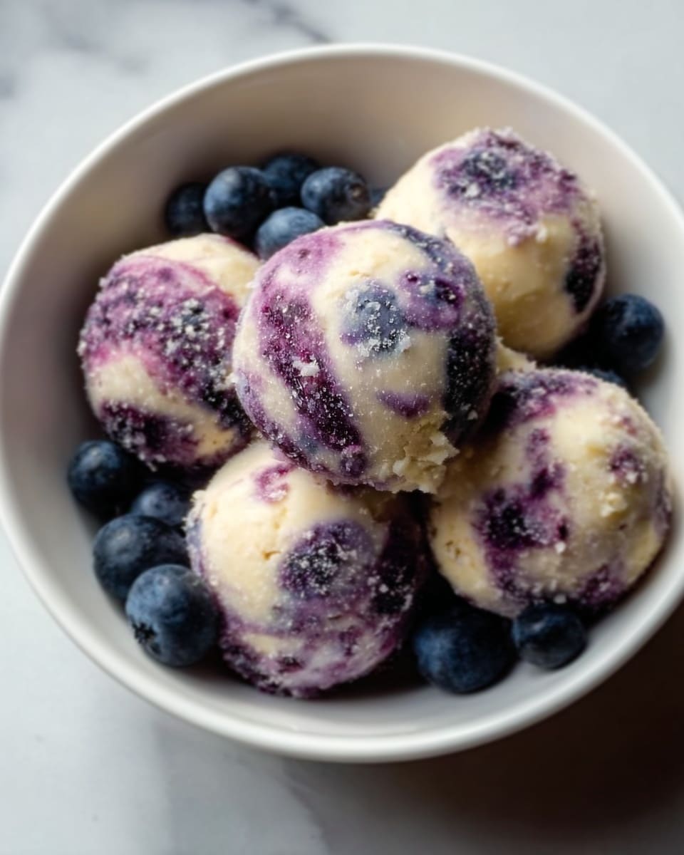 A white bowl holds five round dumplings that are covered in a mix of white dough and purple specks, with a slightly rough, powdery texture. Around the dumplings, there are a few fresh blueberries scattered, adding a deep blue color contrast. The dumplings have a soft, smooth appearance with the purple swirls blending unevenly with the creamy white dough. The background is a white marbled surface that highlights the colors of the food. photo taken with an iphone --ar 4:5 --v 7