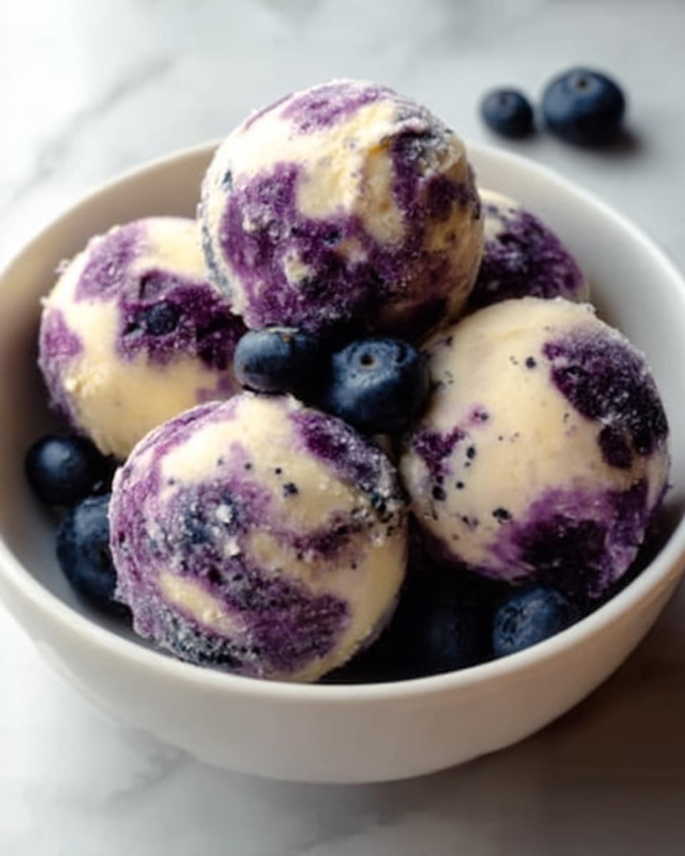 A white bowl holds five round balls with a creamy white base, swirled with purple patches throughout, giving a marbled look. The texture of the balls looks soft and smooth, with some small dark specks scattered on the surface. A few fresh blue blueberries sit around the balls inside the bowl, adding a pop of deep blue color. The background is a white marbled surface, making the colors of the dish stand out clearly. photo taken with an iphone --ar 4:5 --v 7