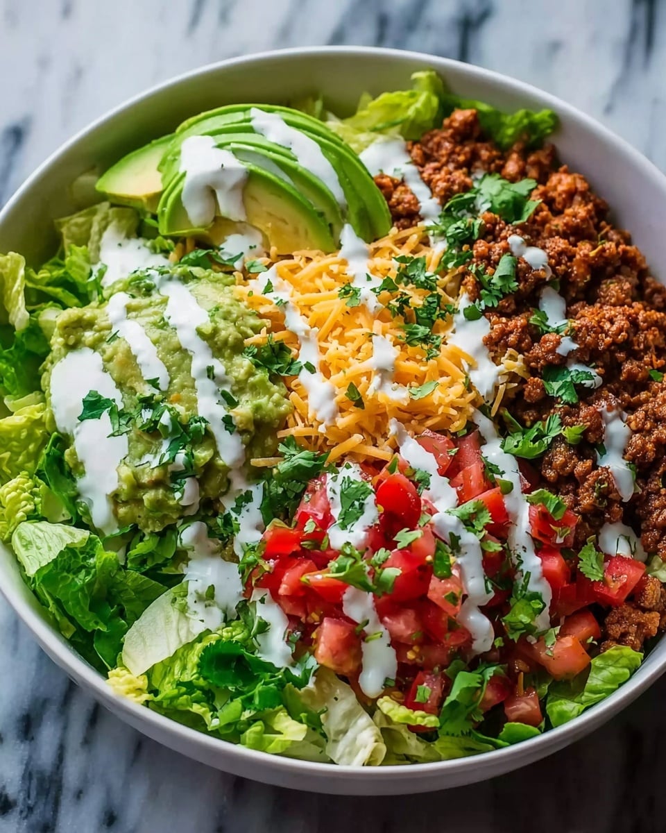 The image shows a large white bowl filled with a colorful layered dish. The bottom layer is fresh green lettuce leaves, slightly torn. On one side, there is a portion of cooked seasoned ground meat with a brown texture. Next to it is a creamy green layer of guacamole, topped with white creamy sauce and some cilantro leaves. Another layer has bright red diced tomatoes mixed with chopped herbs, and shredded yellow cheddar cheese sits in the middle. Thin slices of avocado are placed on one edge. The dish is finished with drizzles of white sauce scattered over all layers and sprinkled fresh green cilantro, all set on a white marbled surface. Photo taken with an iphone --ar 4:5 --v 7