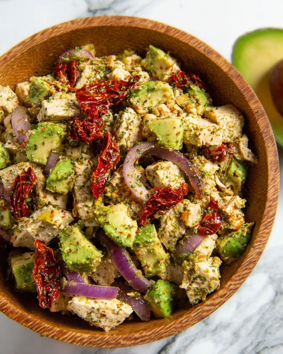 The image shows a wooden bowl full of a mixed dish. The base layer is chunky pieces of light beige cooked tofu with a soft texture, evenly spread throughout the bowl. Mixed within the tofu are bright green chunks of avocado with a smooth, creamy look. There are also thin, curved slices of purple-red onion scattered on top, adding a slight sharp contrast. Bright red sun-dried tomatoes, wrinkled and slightly shiny, are spread evenly across the dish. The entire mix is sprinkled with a fine green herb seasoning, giving a light dusting over the top. The bowl sits on a white marbled surface with an avocado placed nearby. photo taken with an iphone --ar 4:5 --v 7