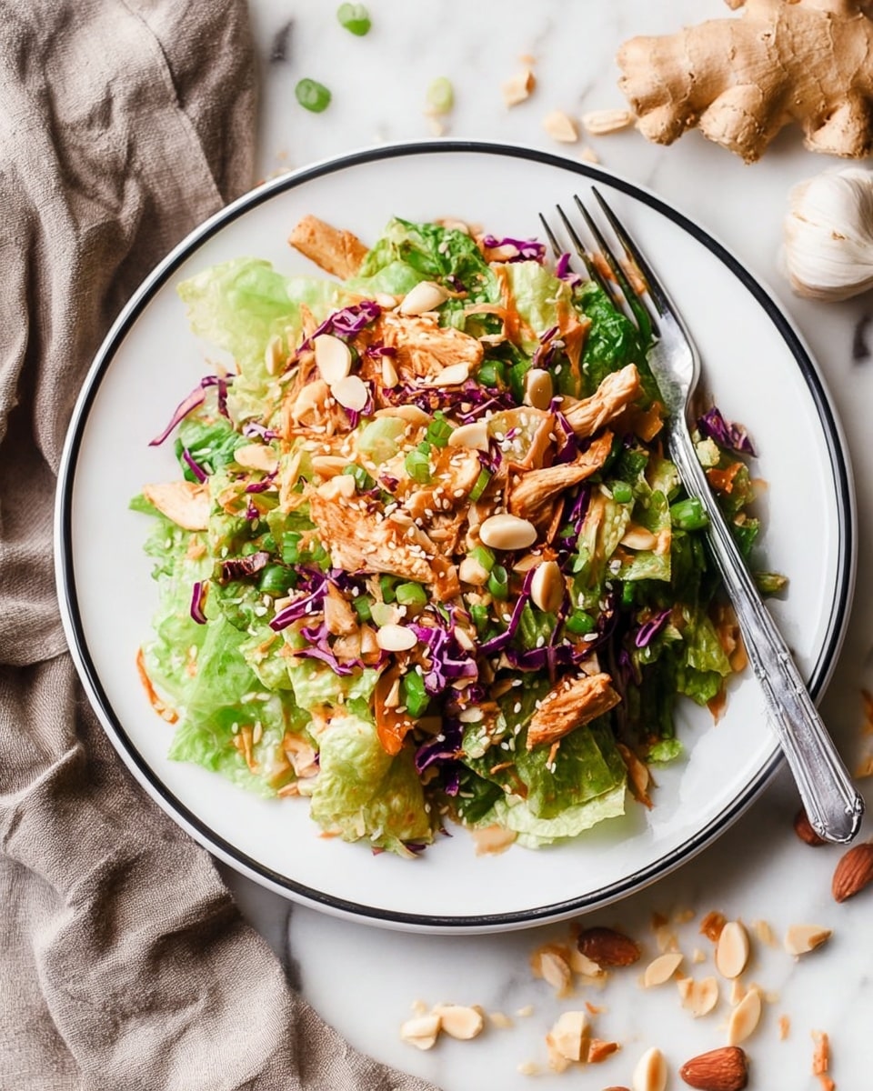 A clear glass bowl sits on a white marbled surface, filled with many layers of colorful salad ingredients arranged separately in sections. On the left, there are small cubes of cooked chicken in light brown and white shades. Above the chicken, bright green chopped spring onions add freshness, next to shredded orange carrots. To the right, thin slices of purple cabbage form a neat pile, beside light tan almond slices. On the bottom right, there are dark brown crispy bacon pieces and fresh green leafy lettuce. A thick, golden-brown dressing is being poured into the center of the bowl, creating a smooth mound that starts to spread over the ingredients. photo taken with an iphone --ar 4:5 --v 7