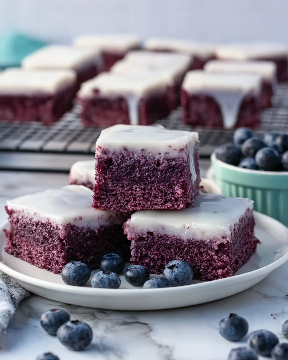 The image shows a white plate with five square-shaped blueberry cake pieces stacked. Each cake piece has two layers: the bottom layer is thick and purple, showing a moist, crumbly texture, while the top layer is a thin, smooth, shiny white icing that slightly drips down the sides. Around the plate, there are fresh blueberries scattered on a white marbled surface, adding color contrast. In the background, more cake pieces are visible on a metal cooling rack. A tray with additional blueberries is on the far right side. photo taken with an iphone --ar 4:5 --v 7